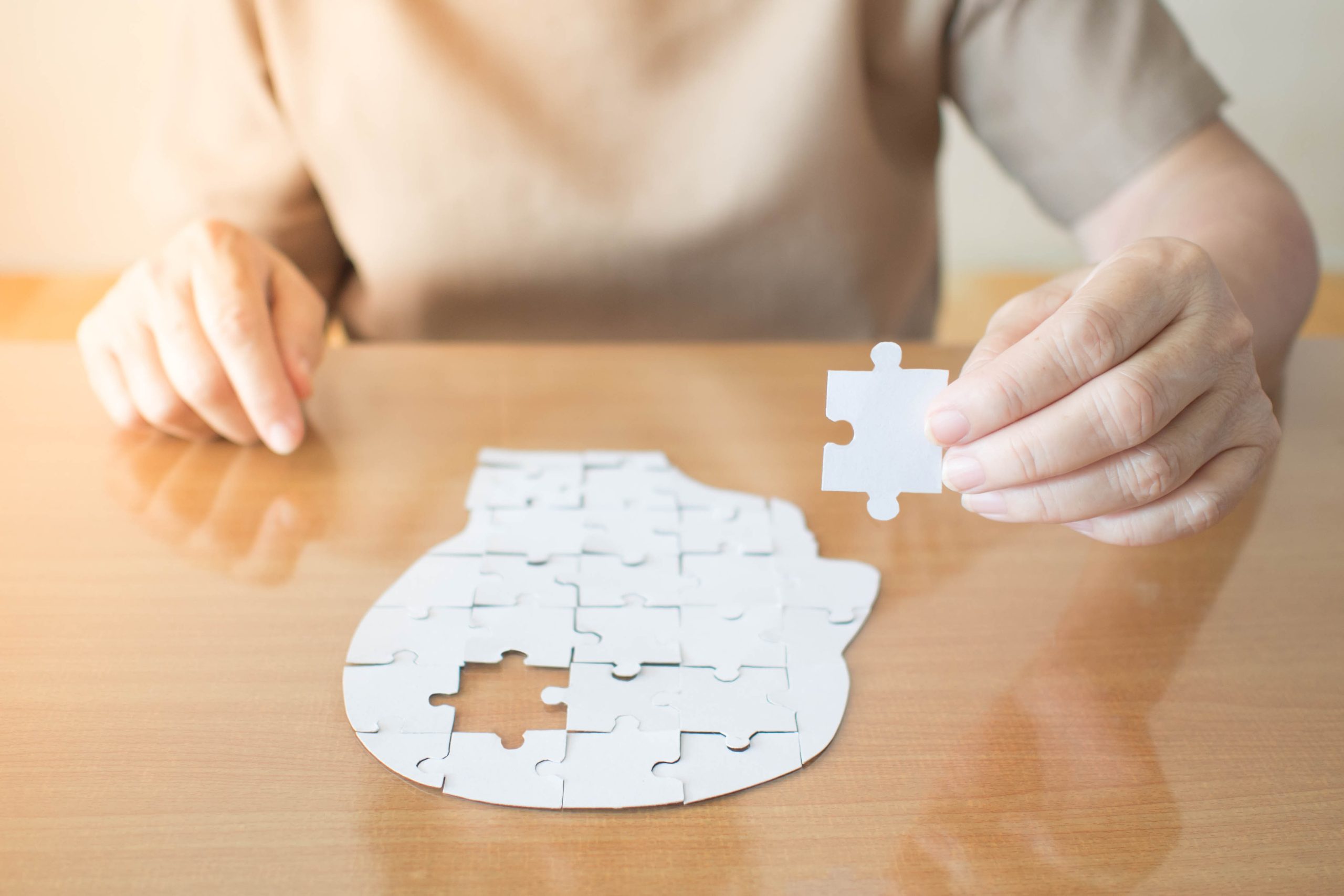 An older lady's hands adding the final piece to a jigsaw representing a human head.