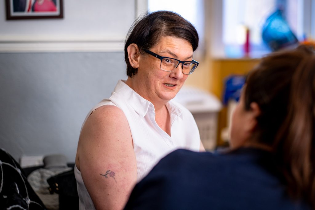 A lady with short dark hair, wearing glasses and a white sleeveless shirt discussing home care with an Apollo Care staff member.